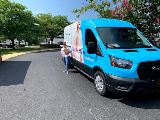 A woman standing next to a blue delivery van on a sunny day.