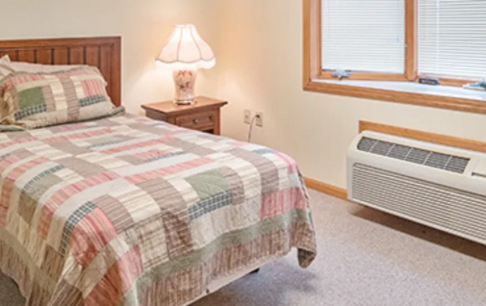 A cozy bedroom with a single bed, bedside lamp, and a quilted bedspread.