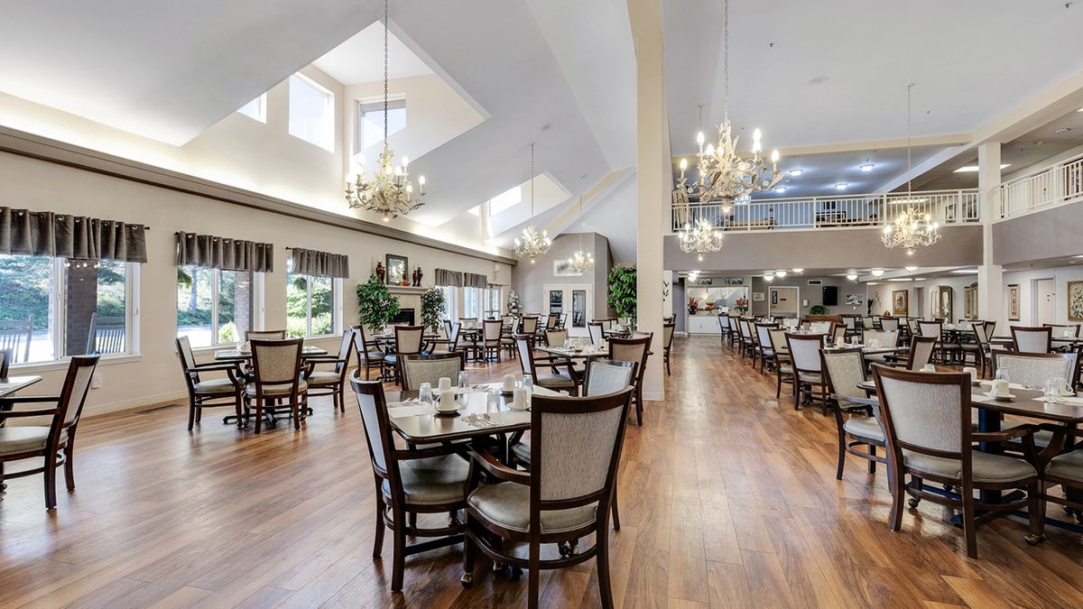 A spacious and elegantly designed dining room with multiple tables and chairs, illuminated by chandeliers and natural light from large windows.