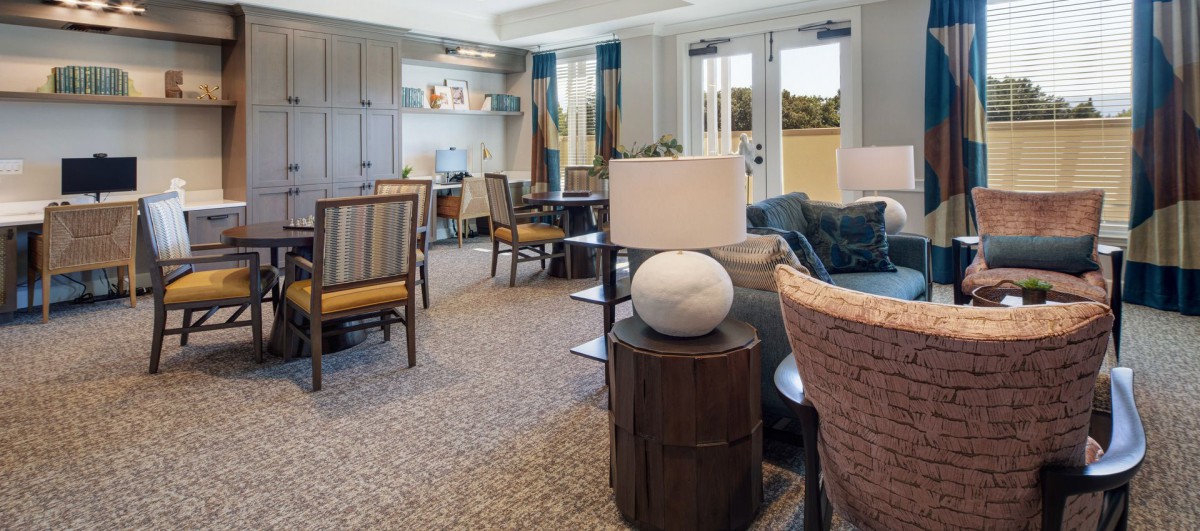 A stylish living room with elegant furniture and decor, featuring a table lamp, chairs, and large windows.