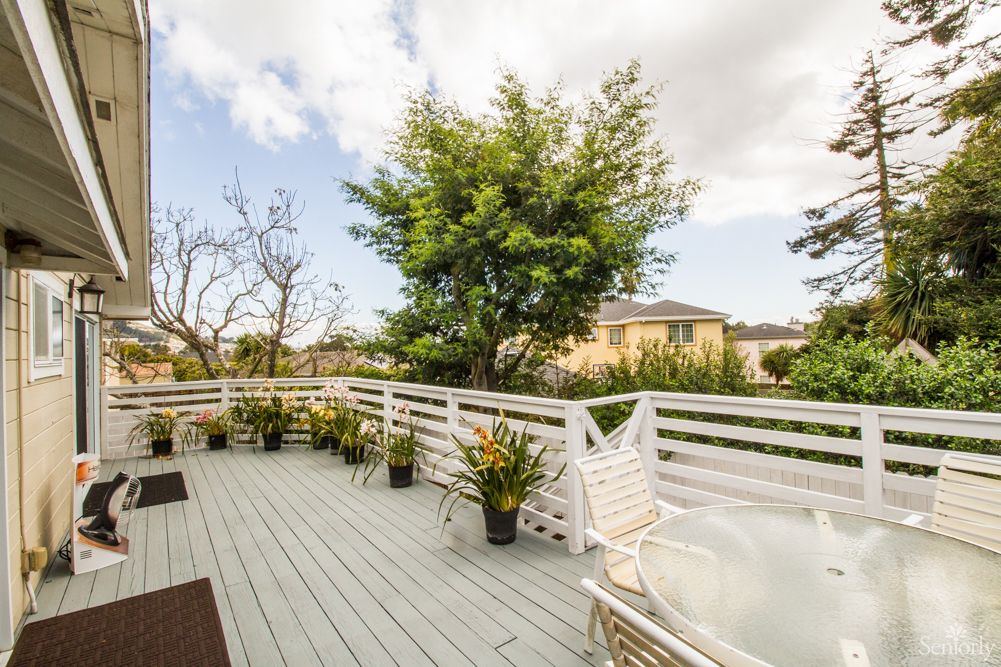 A spacious outdoor deck with potted plants and a view of trees in the background.