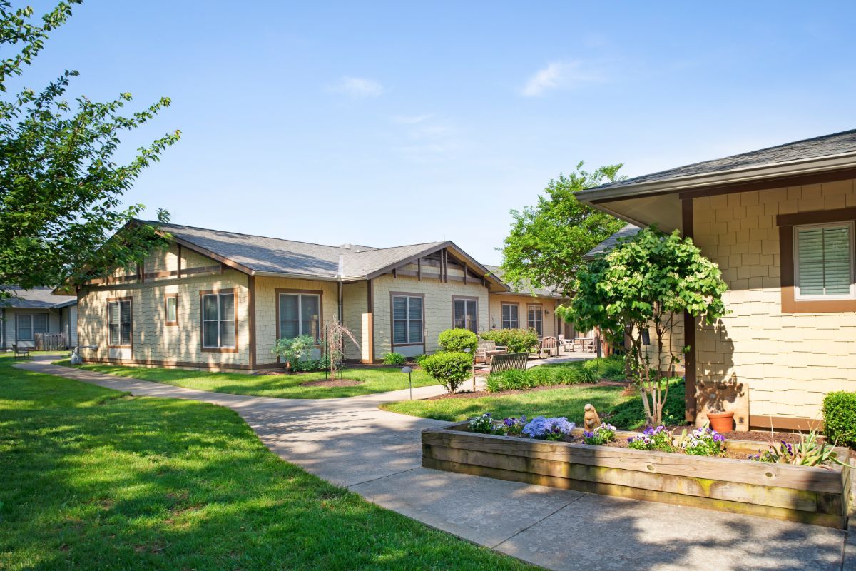 A serene outdoor landscape featuring buildings surrounded by lush greenery and a well-maintained garden.