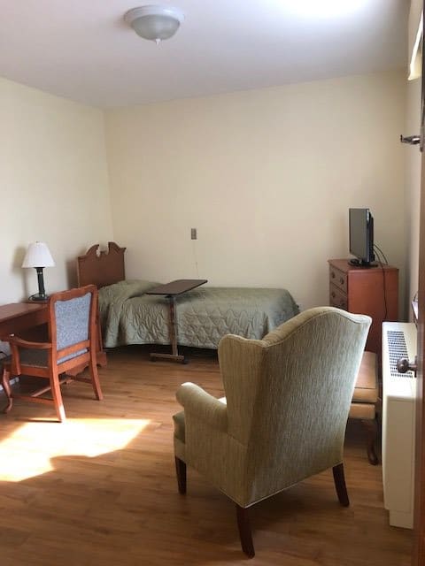 A simple bedroom with a single bed, a desk, and a television.