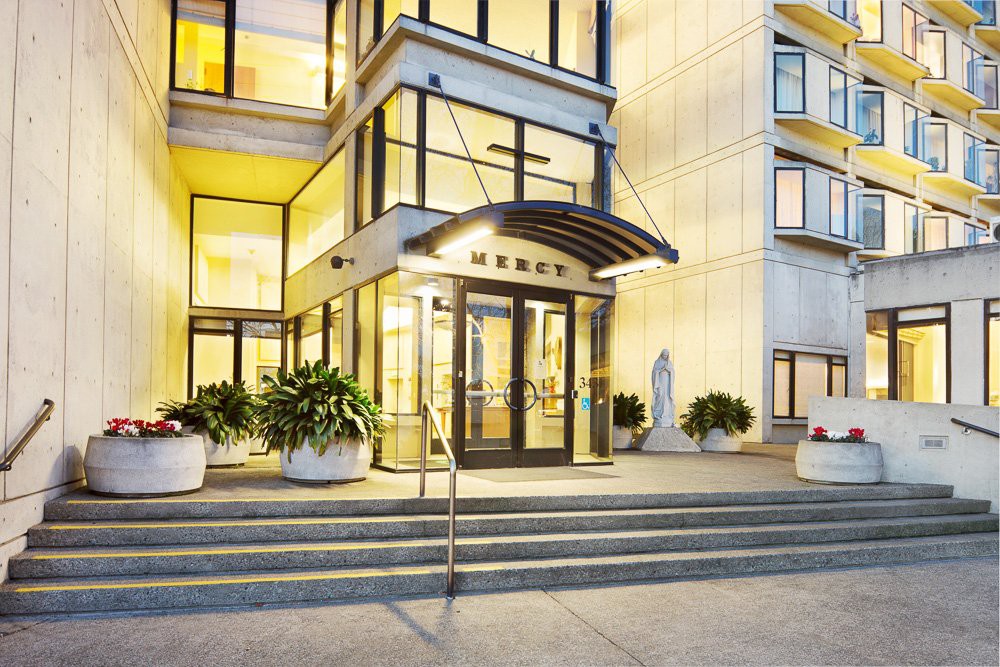 A modern building entrance with glass doors, steps, and decorative plants.