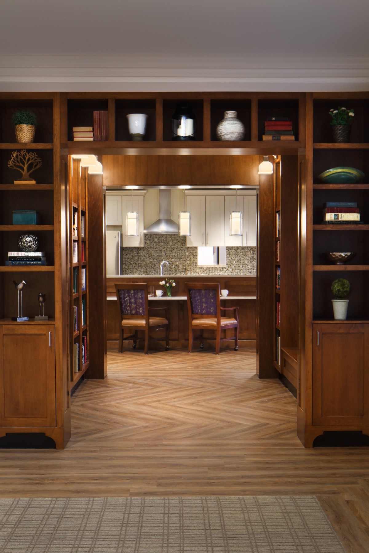 A cozy kitchen viewed through a room lined with wooden bookshelves.