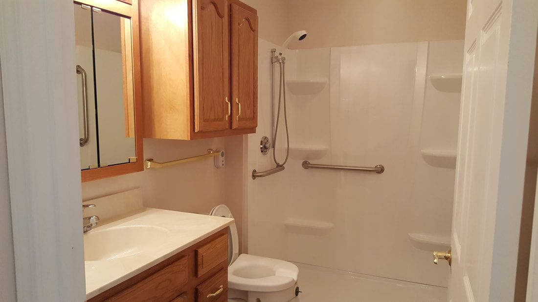 A bathroom featuring a shower with grab bars, wooden cabinets, and a toilet.