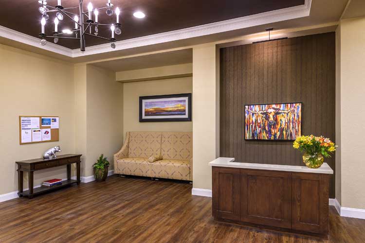A well-decorated lobby with a sofa, chandelier, paintings, and a wooden floor.