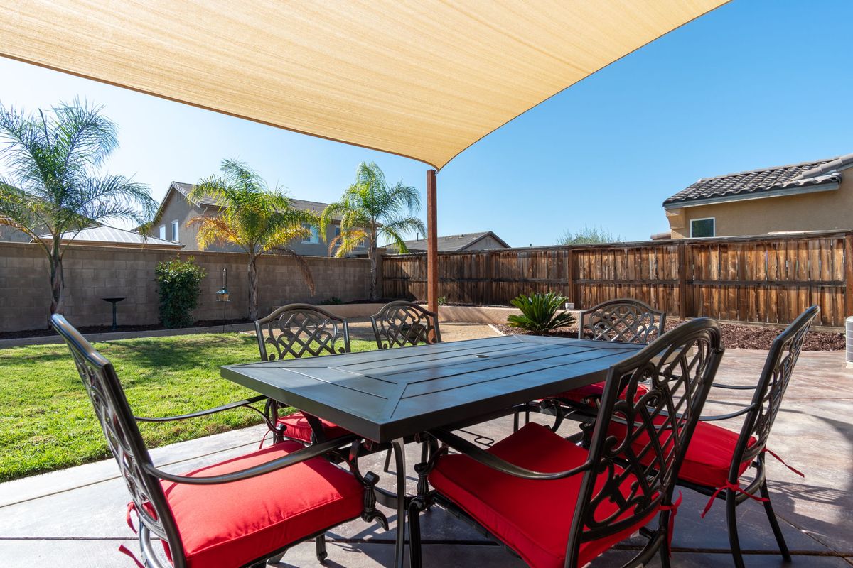 A sunny backyard patio with a table and chairs under a shade sail.