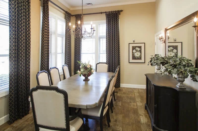Elegant dining room with a long table, surrounded by chairs and illuminated by a chandelier.