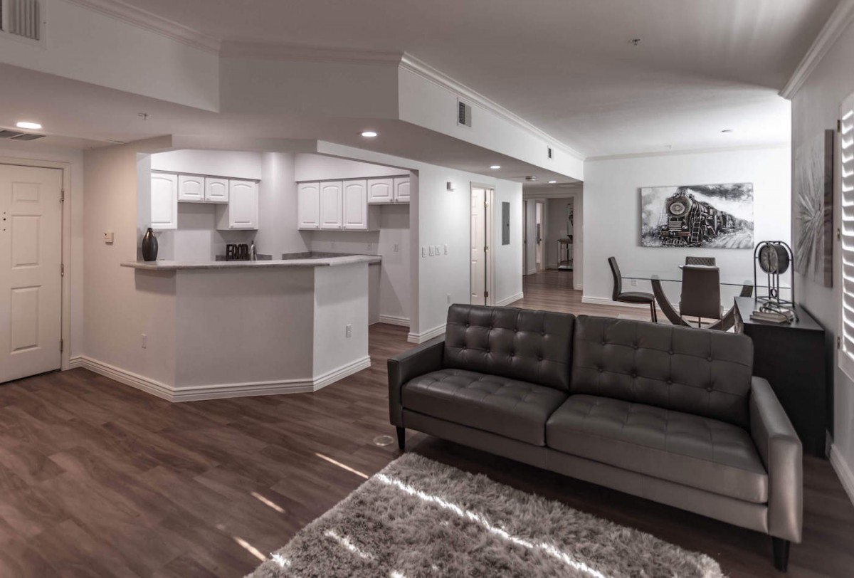 A modern open floor plan featuring a living room with a grey sofa, a kitchen with white cabinets, and a dining area.