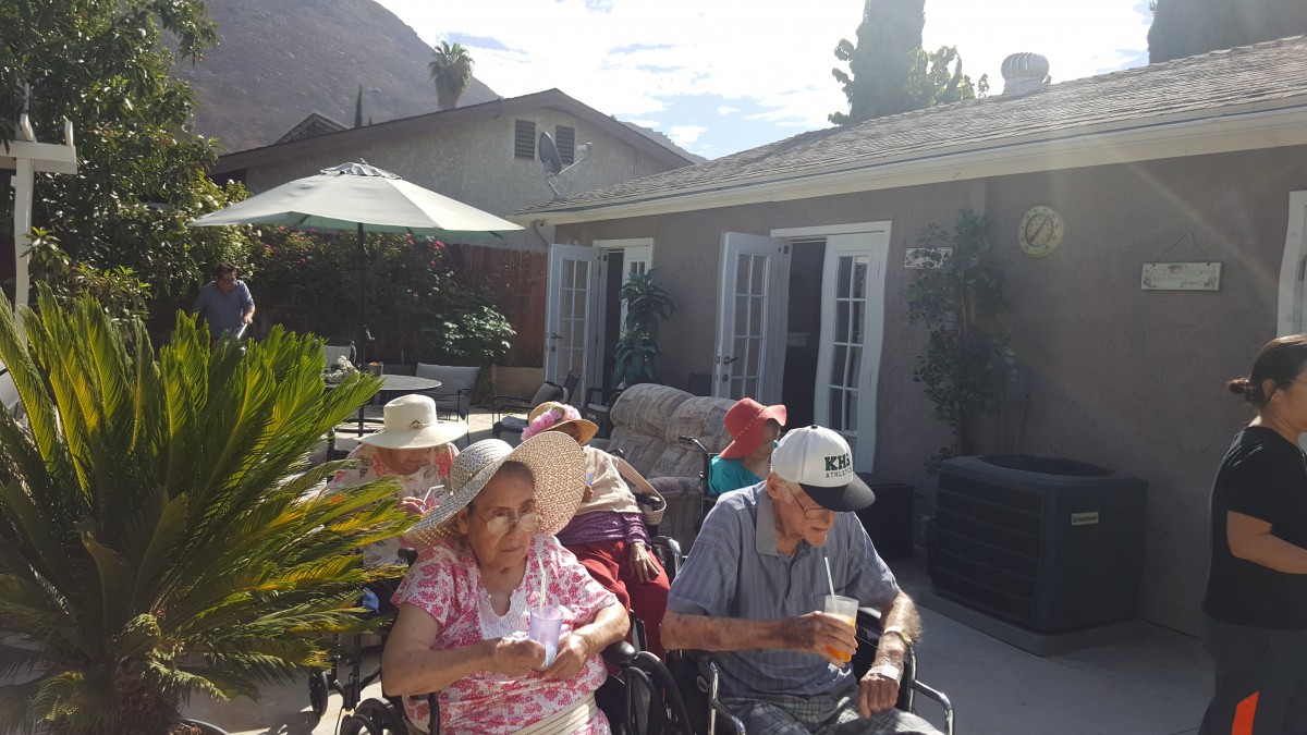 A group of seniors enjoying a sunny day on a patio, seated in wheelchairs and wearing hats.