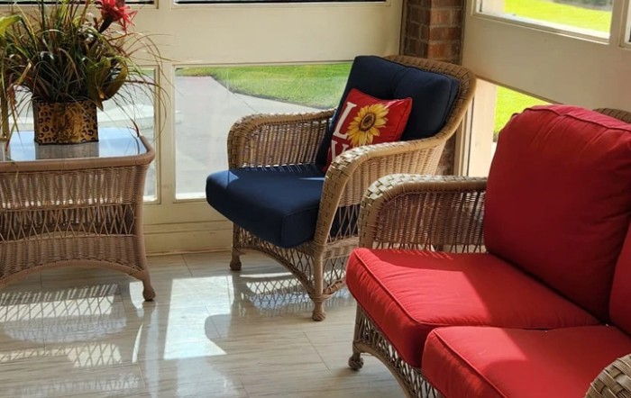 A sunlit room featuring wicker chairs with colorful cushions and a decorative pillow.