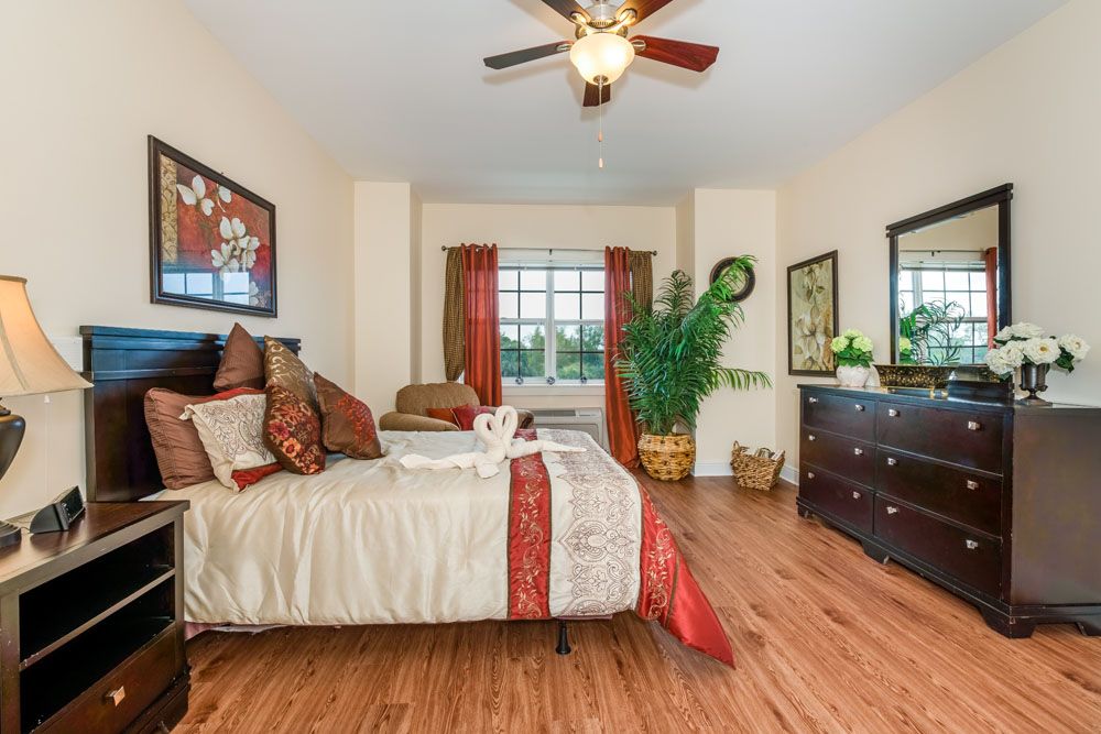 A cozy bedroom with elegant decor, featuring a bed, ceiling fan, artwork, and large window.