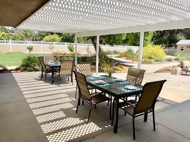An outdoor patio with a pergola, featuring tables and chairs set for dining.