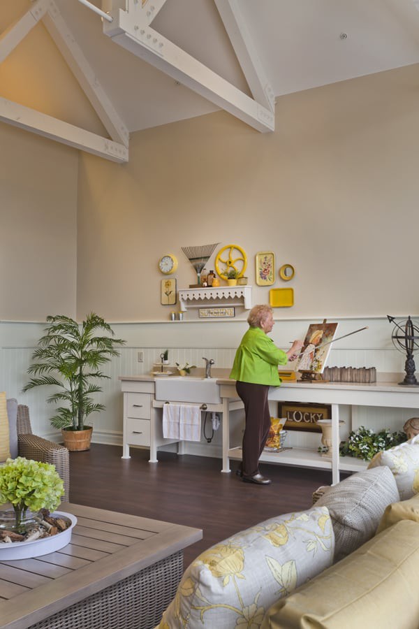 An artist works in a bright and well-organized art studio, surrounded by plants and creative tools.