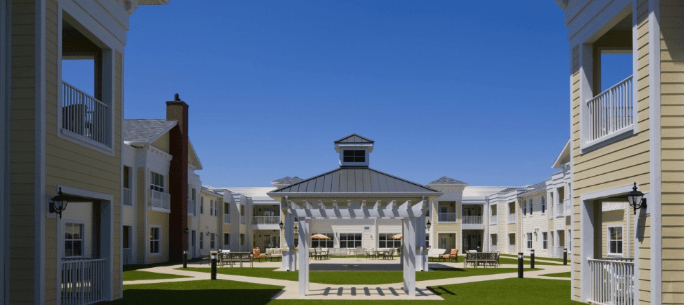 A modern building with a central pergola in an open courtyard under a clear blue sky.