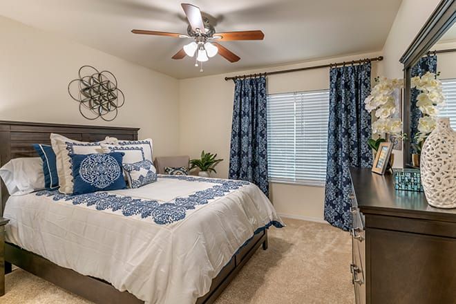 A cozy bedroom with blue and white decor, featuring a bed, curtains, wall art, and a ceiling fan.