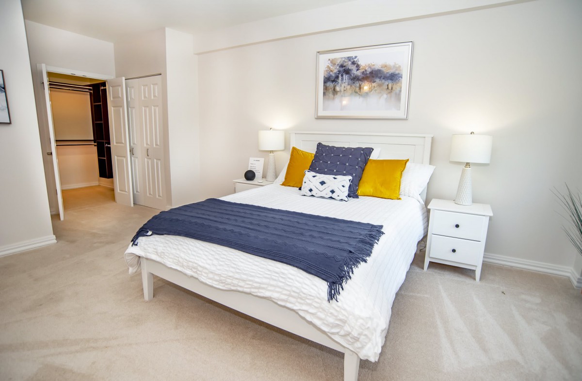 A modern and cozy bedroom featuring a white bed with decorative pillows, flanked by nightstands and lamps, complemented by wall artwork.