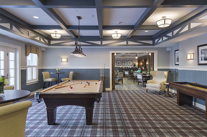 A cozy recreation room featuring a pool table with overhead lighting and a plaid carpet.