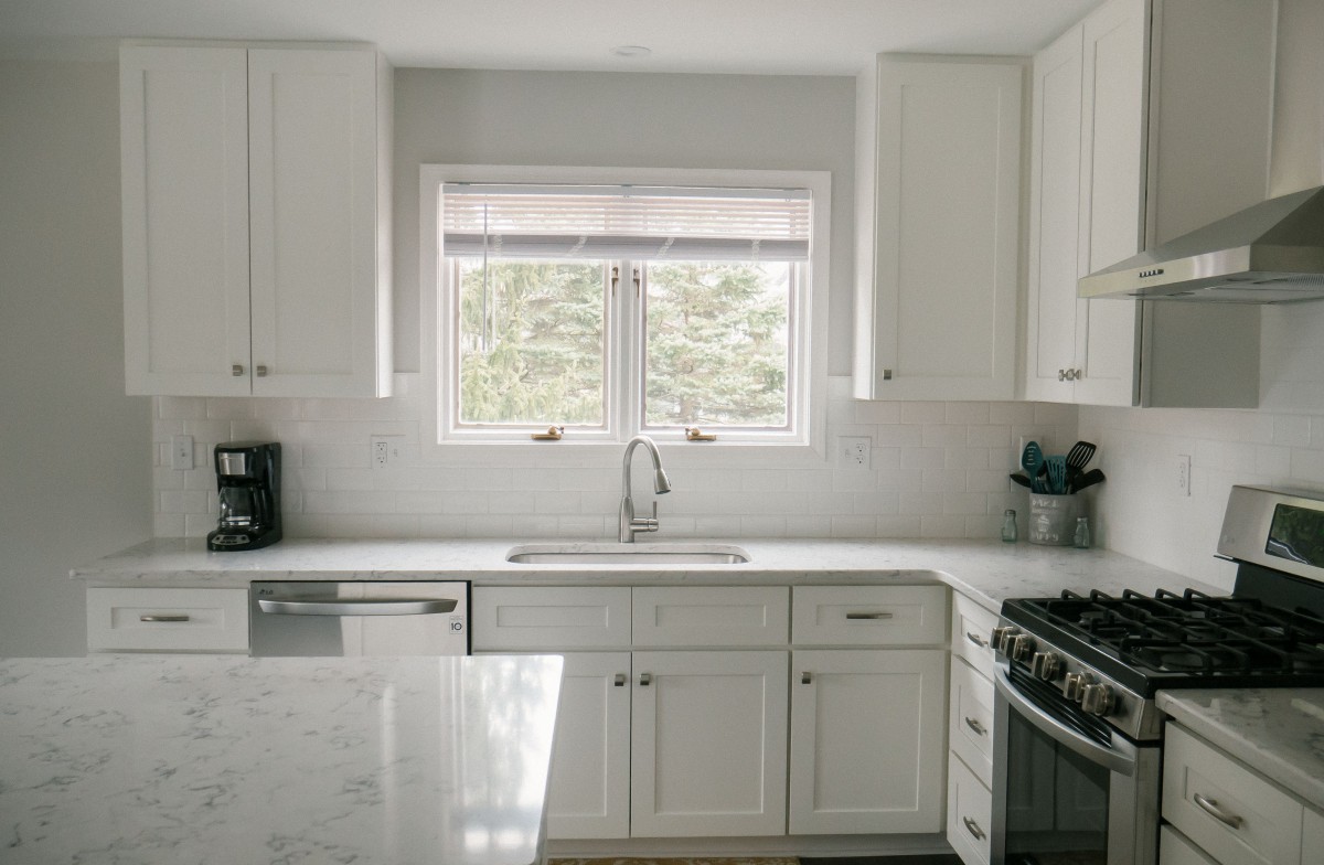 A modern kitchen with white cabinets and a central window.