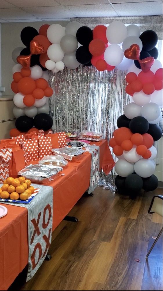 A festive party setup with colorful balloon decorations and a table covered in orange-themed items.