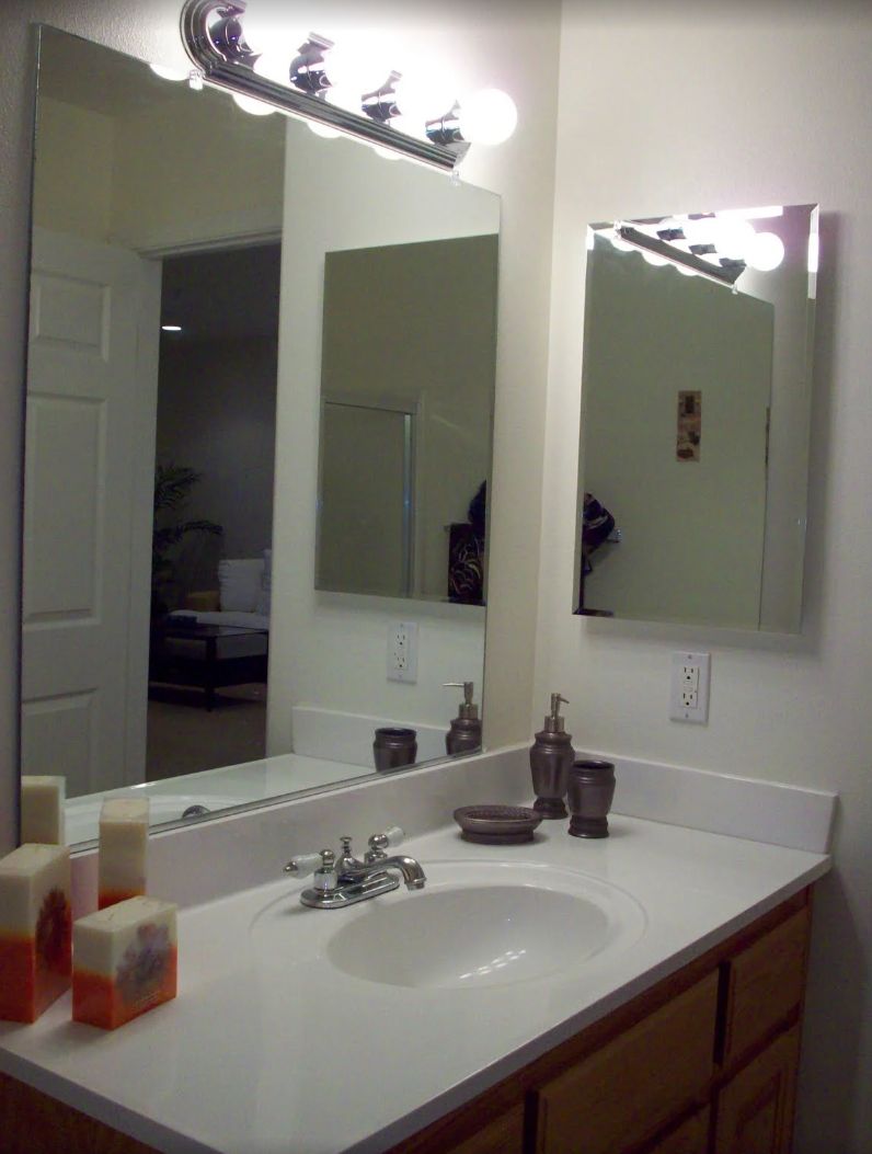A clean bathroom with a sink, mirror, and soap dispensers on the countertop.