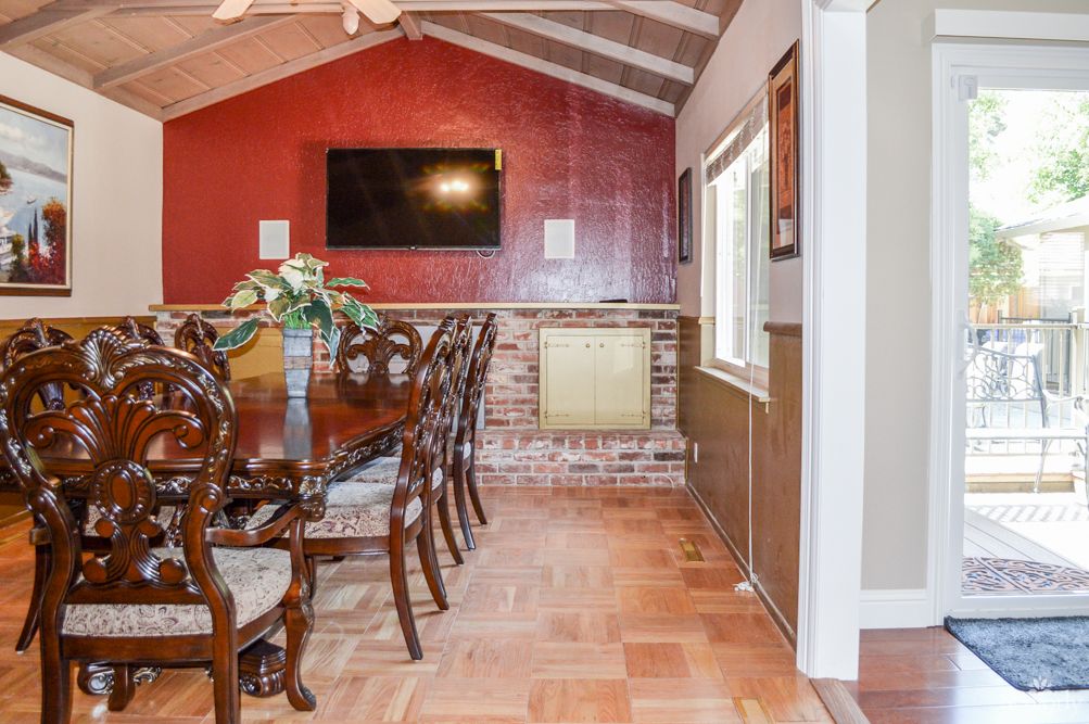 A cozy dining room with a wooden table, elegant chairs, and a brick accent wall featuring a mounted television.