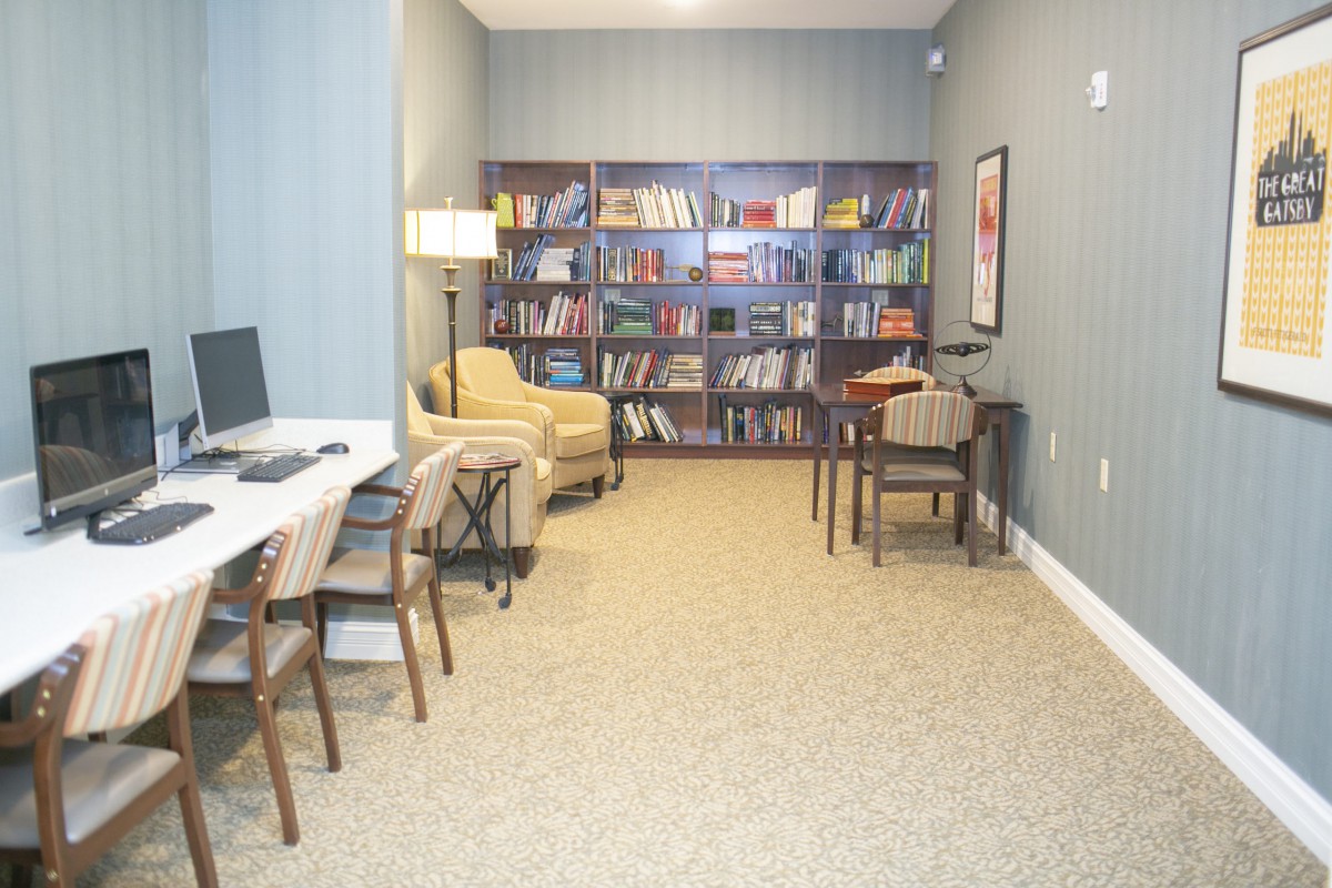 A cozy library room with bookshelves, seating, and a computer desk.