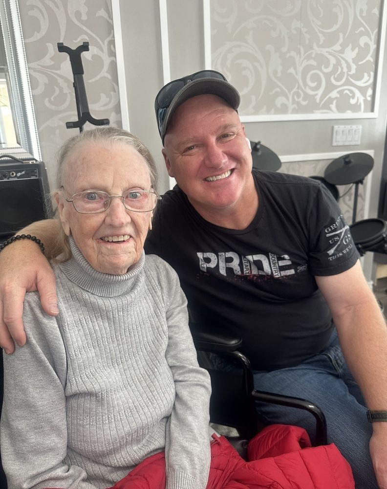 An elderly woman and a man smiling together indoors.