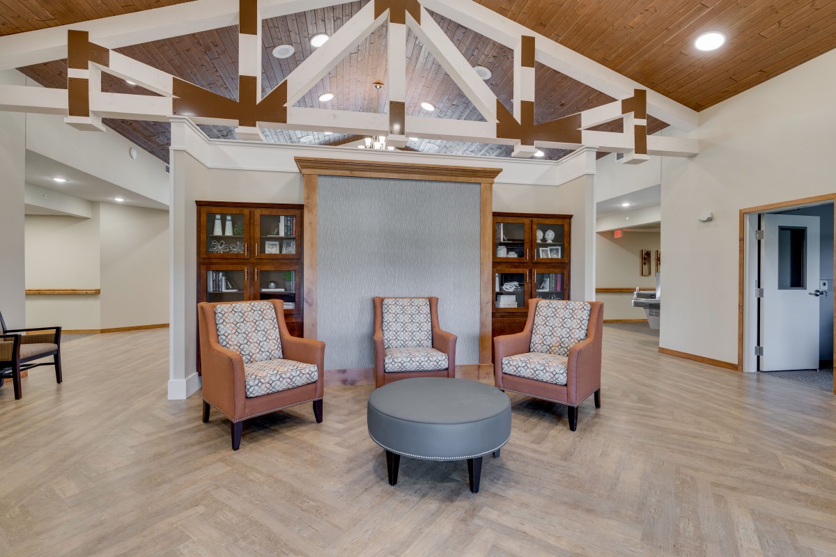 A modern lobby with upholstered chairs and a round table, framed by bookshelves and decorative beams.