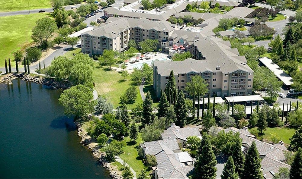Aerial view of residential buildings surrounded by lush greenery and a nearby river.