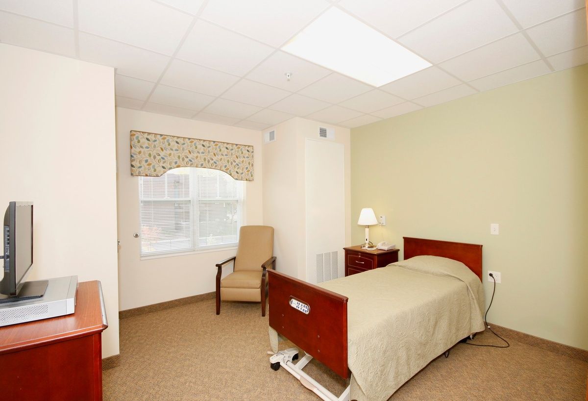 A clean and minimalist hospital room with a single bed, chair, and lamp.