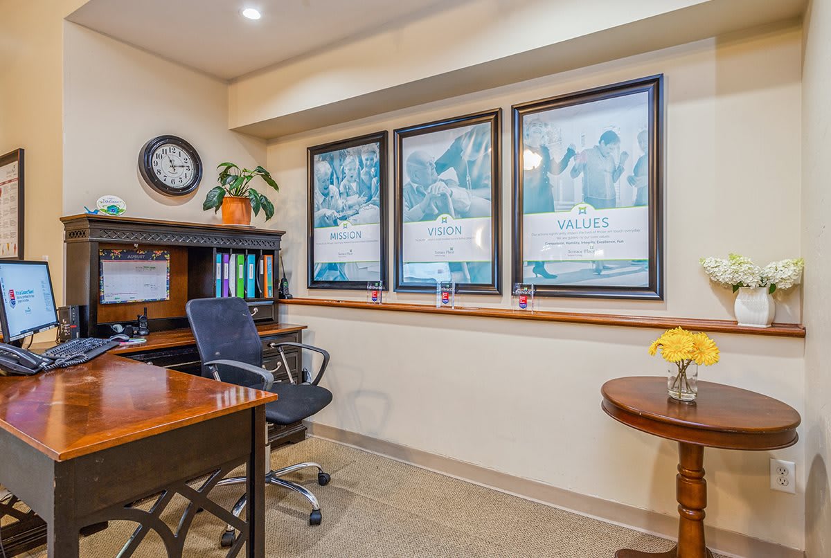 A neatly arranged office space with a desk, chair, framed artwork, and a wall clock.