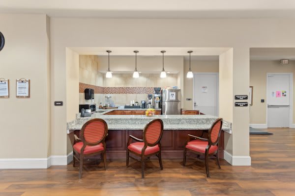 A modern kitchen with a countertop, red cushioned chairs, and pendant lighting.