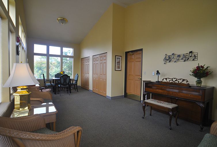 A spacious room with a piano, seating area, and large windows providing natural light.