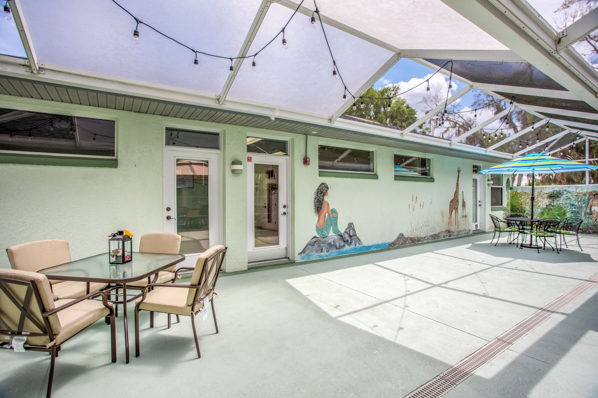 A cozy patio area with string lights, featuring outdoor seating and a vibrant mural on green walls.
