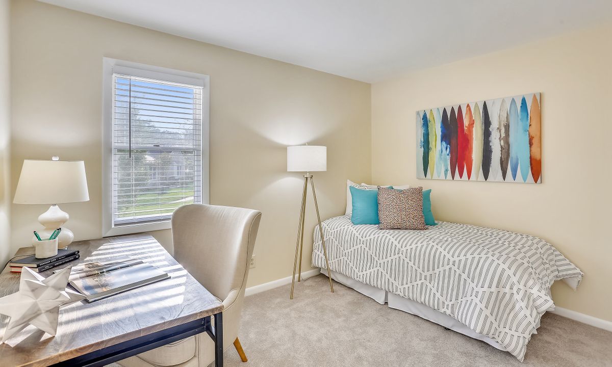 A minimalist bedroom with a daybed, desk, and colorful artwork.