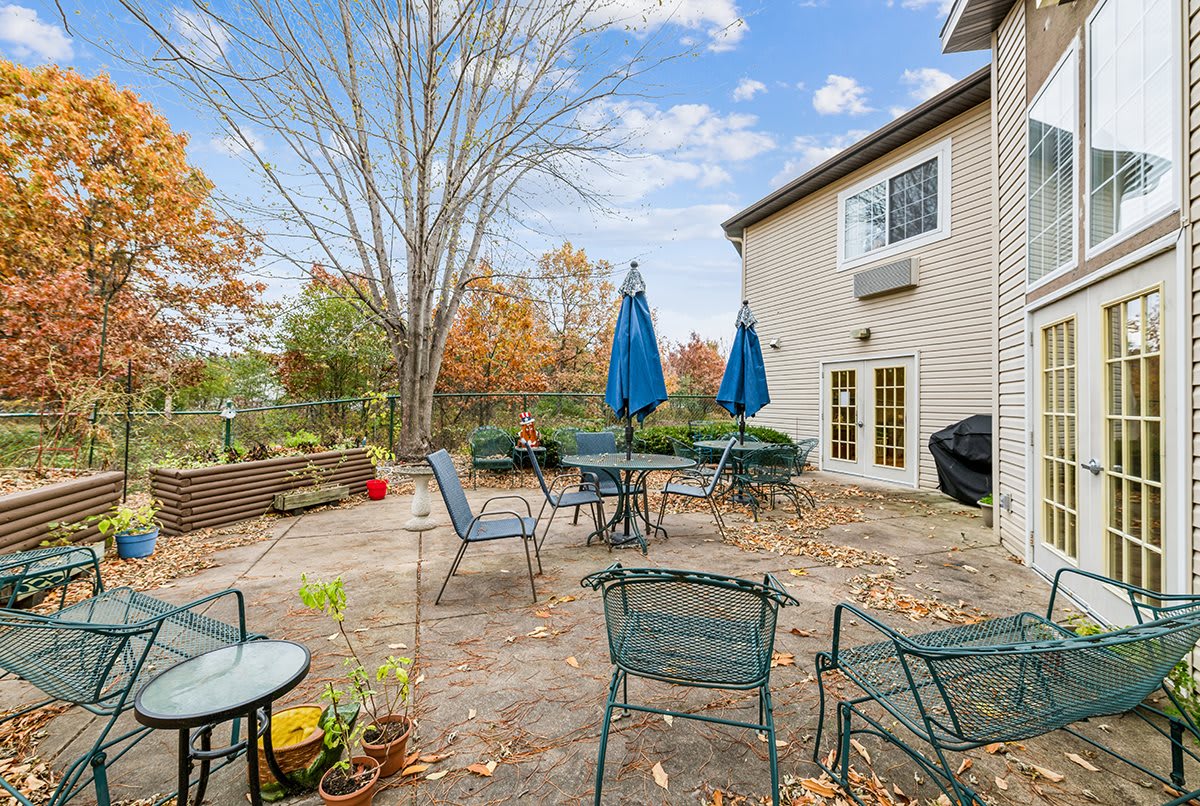 A backyard patio with tables, chairs, and umbrellas set against an autumn landscape.