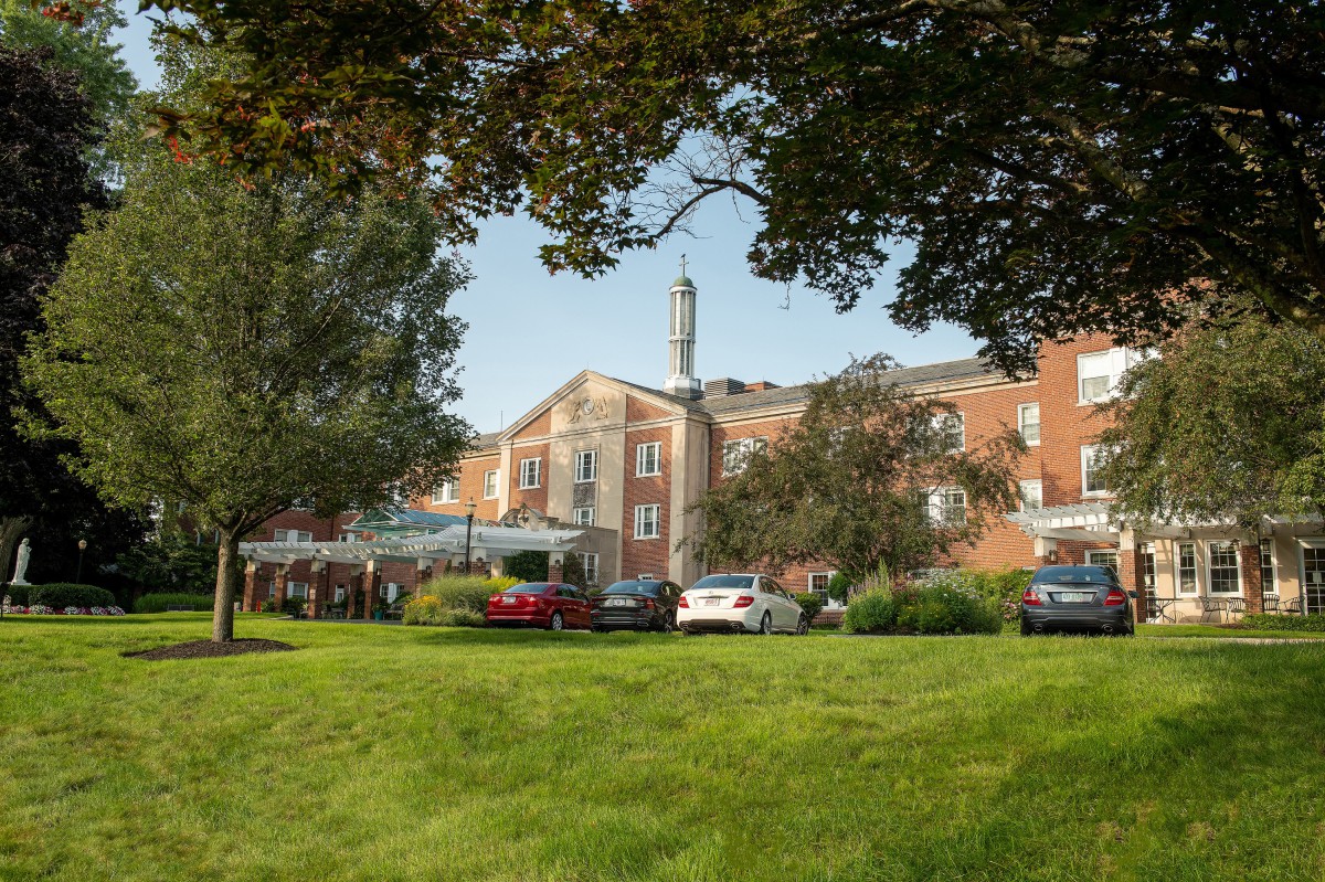 A hotel building surrounded by lush greenery and parked cars on the lawn.