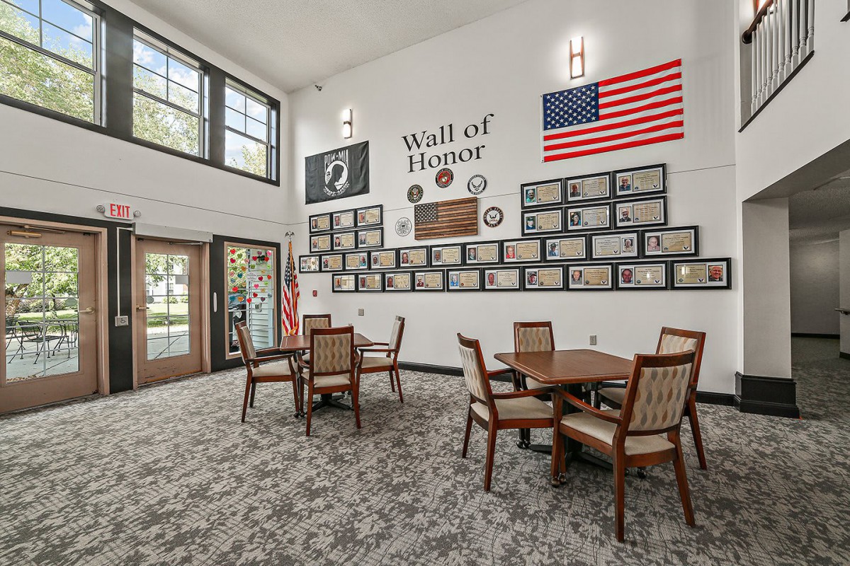 A room with a Wall of Honor featuring framed photos, American flags, and seating area.