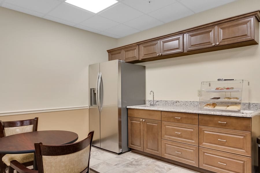 A modern kitchen with wooden cabinets, a stainless steel refrigerator, and a small dining area.