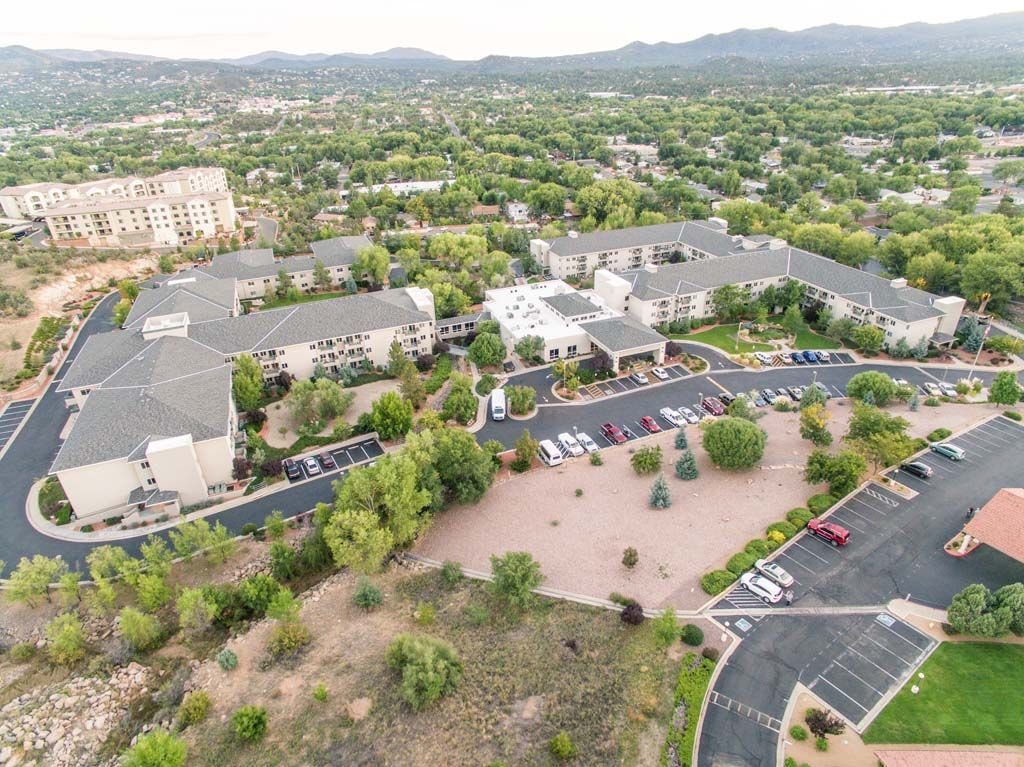 Aerial view of a complex with buildings, parking lots, and surrounding greenery set against a backdrop of mountains.