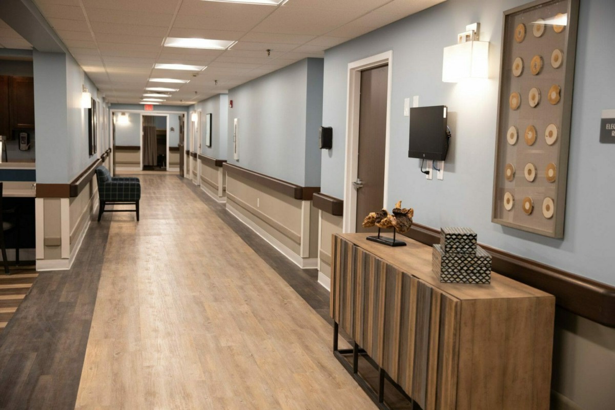 A clean and modern hospital corridor with light wooden flooring, wall decor, and seating area.