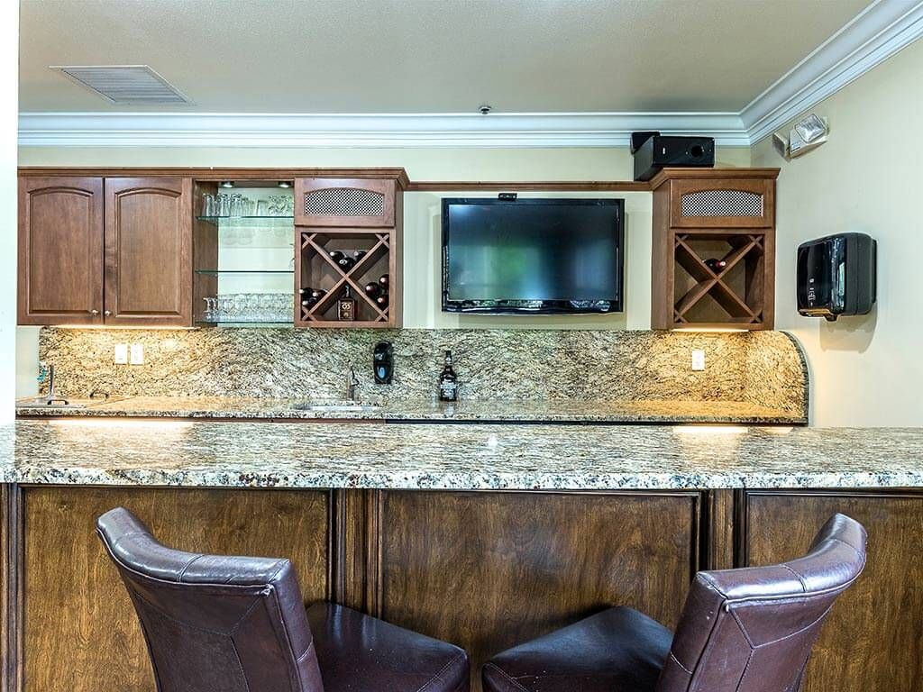 A stylish home bar area featuring a granite countertop, wooden cabinets with wine racks, and comfortable seating.