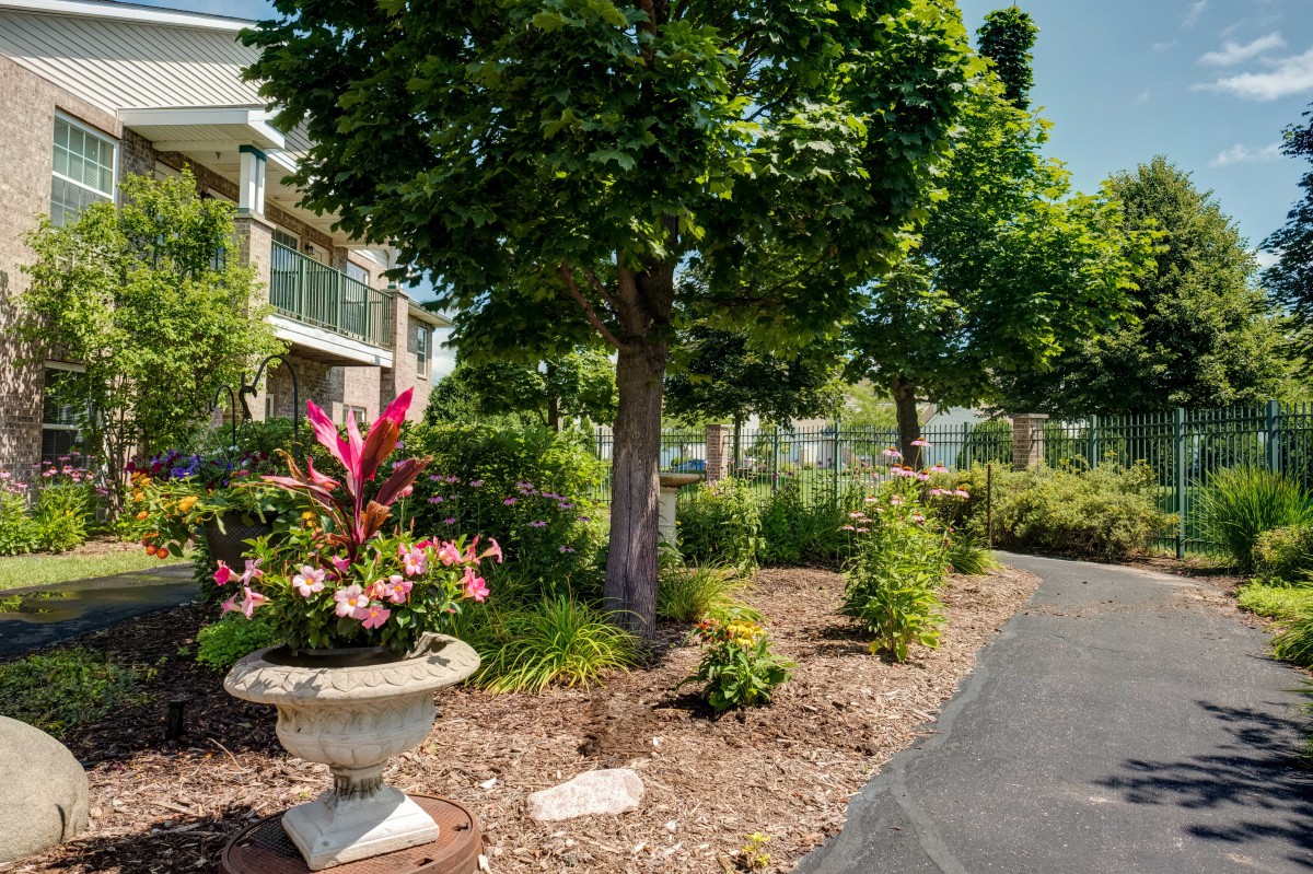 A landscaped garden with lush trees and vibrant flowers lining a paved pathway.