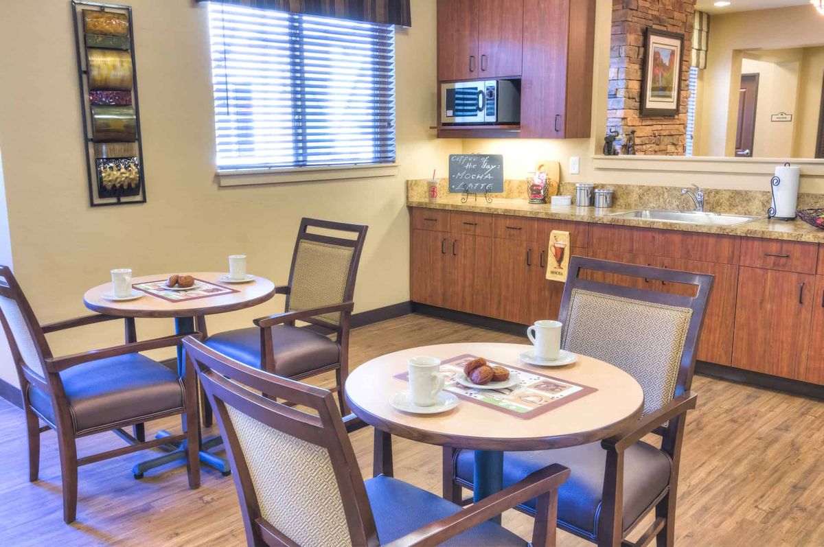 A cozy dining area with a kitchenette and several round tables set for meals.