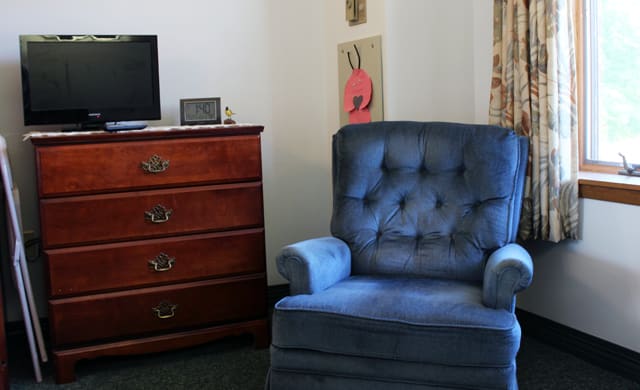 A cozy living room corner with a blue armchair and a wooden dresser next to a small television.