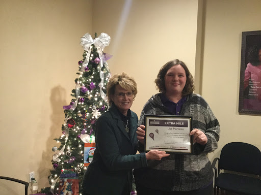 Two individuals celebrate an achievement with a certificate in front of a decorated Christmas tree.
