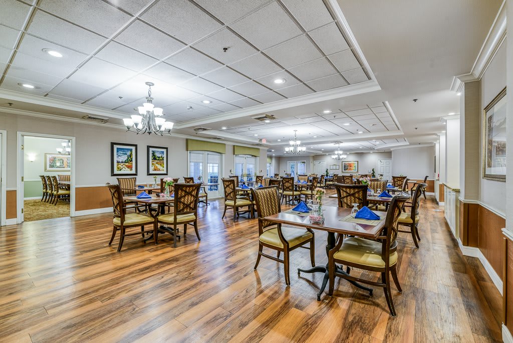 A spacious and elegantly furnished dining room with neatly arranged tables and chairs, featuring bright lighting and wooden flooring.