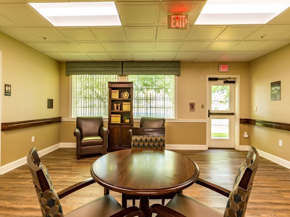 A cozy seating area with a round table and chairs, featuring a bookshelf and large window.